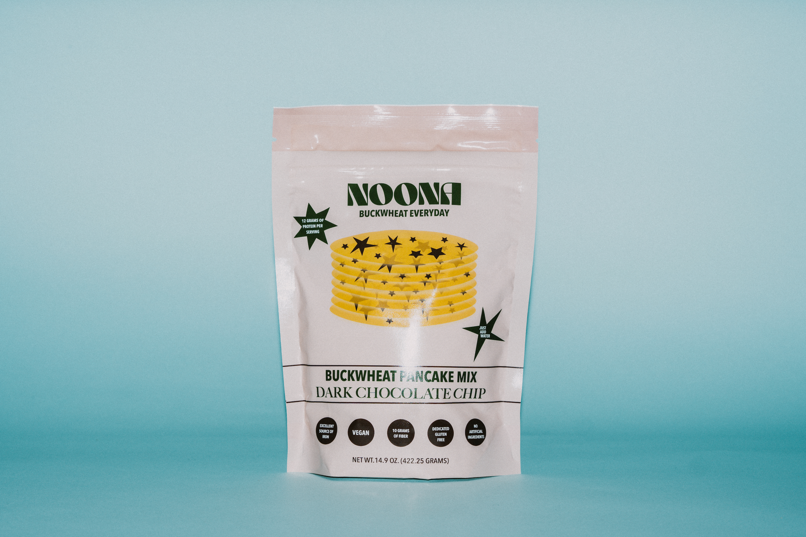 A front view of Noona's Dark Chocolate Chip Buckwheat Pancake Mix packaging. The stand-up pouch features a clean, modern design with earthy tones that reflect its natural ingredients. The Noona logo is prominently displayed at the top, along with the product name: "Dark Chocolate Chip Buckwheat Pancake Mix." Below, a tagline reads: "Gluten-Free | Vegan | High Protein | Kosher." The packaging also highlights the key selling points: made with real ingredients, no artificial flavors